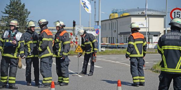 Einsatzkräfte der Feuerwehr an der Zufahrt zur Raffinerie. Einer stellt einen Schild auf, das vor Strahlung warnt. Foto: Andre Lenthe Fotografie Zwei Verletzte Arbeiter bei Strahlenunfall