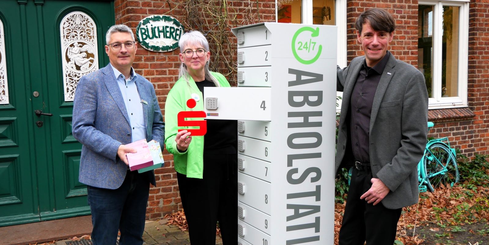 Nikola Laudien, Leiterin der Gemeindebücherei Stelle, freut sich gemeinsam mit Dr- Aleander Stark (Landkreis Harburg) und Stefan Bültemann (Sparkasse Harburg-Buxtehude) über die neue Abholstation. Foto: Sparkasse