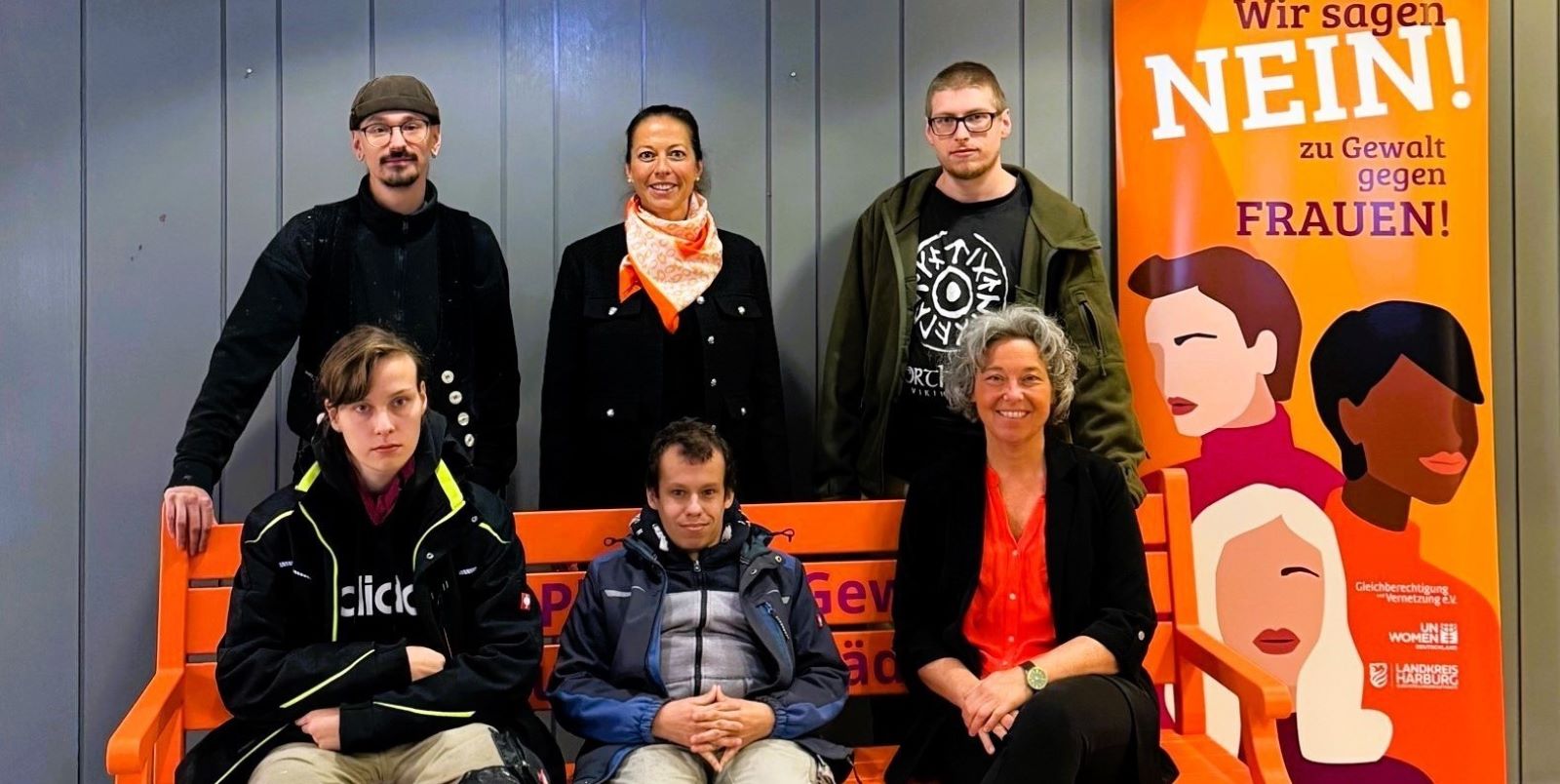 Die neue orangefarbene Bank im Kreishaus ist ein sichtbares Zeichen gegen Gewalt gegen Frauen, die die Beschäftigte der Lebenshilfe, Kreisrätin Ana Cristina Bröcking (stehend, Mitte) und Gleichstellungsbeauftragte Andrea Schrag (sitzend, rechts) aufgestellt haben. Foto: Landkreis Harburg